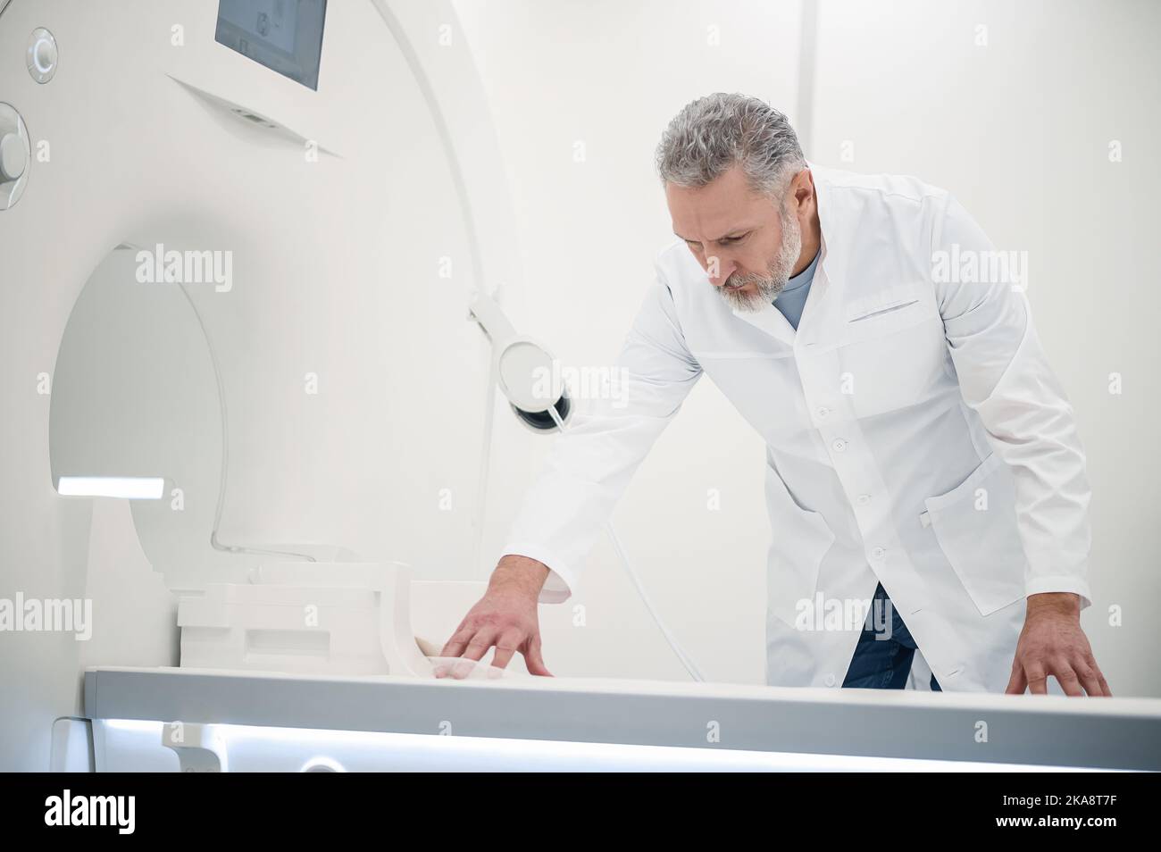 Male gray-haired doctor in a lab coat preparing MRI scanner Stock Photo