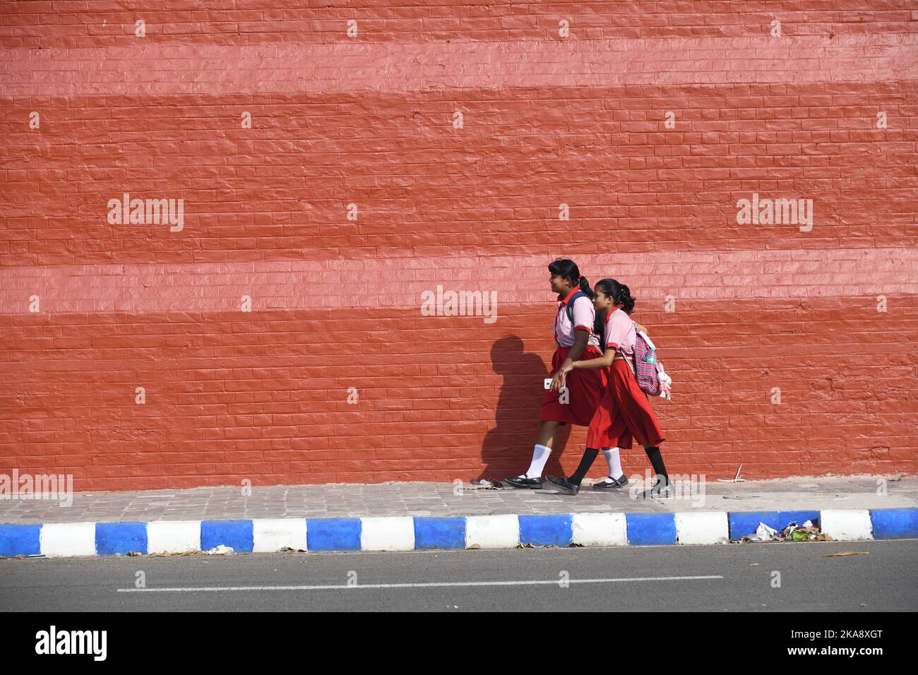 Two schoolgirls walking against red boundary wall of Alipore Jail Museum. Kolkata, West Bengal, India. Stock Photo