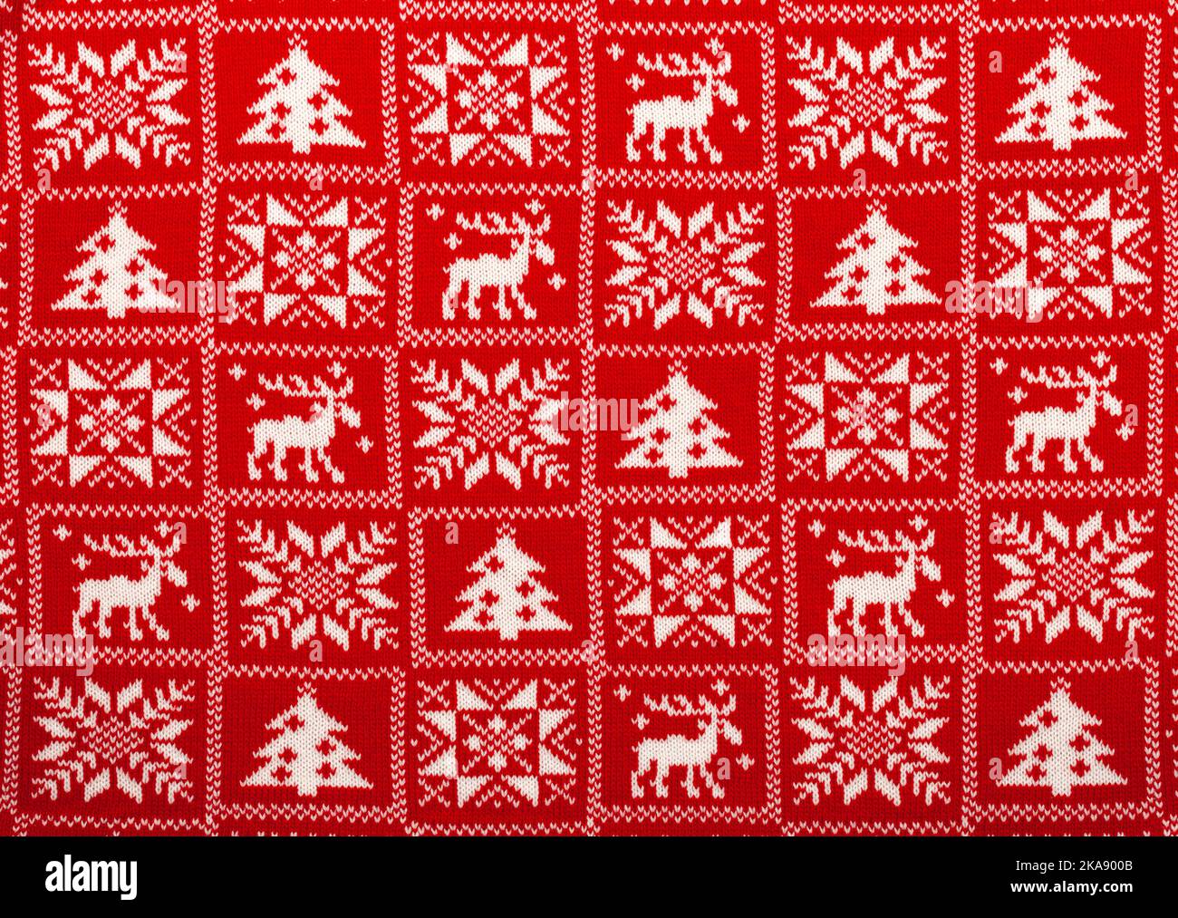 Red knitted fabric with white moose, fir tree and snowflake Scandinavian style geometric ornament cristmas background Stock Photo