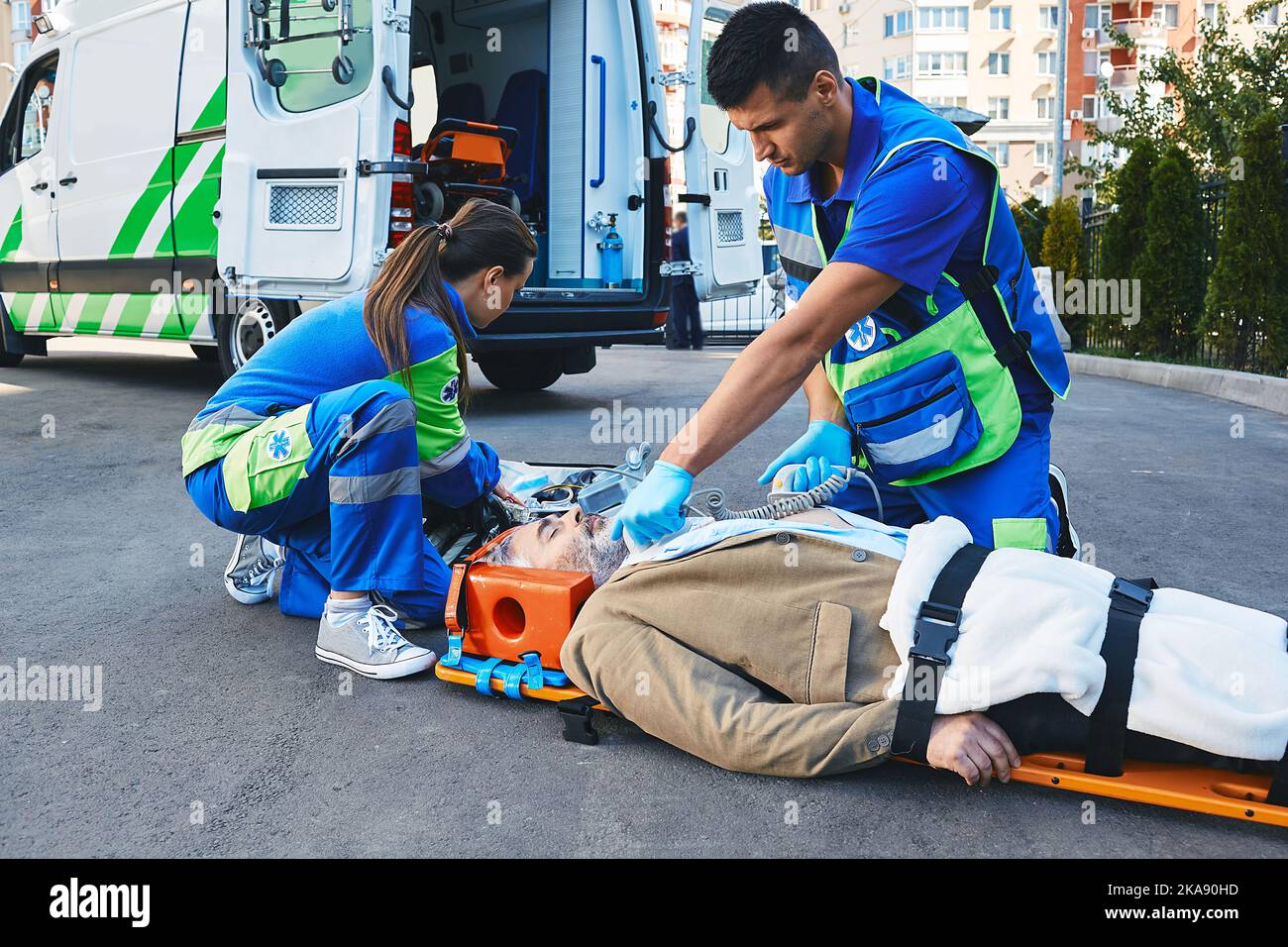 Ambulance paramedic with defibrillator performing cardiopulmonary resuscitation on cardiac patient lying on emergency stretcher Stock Photo