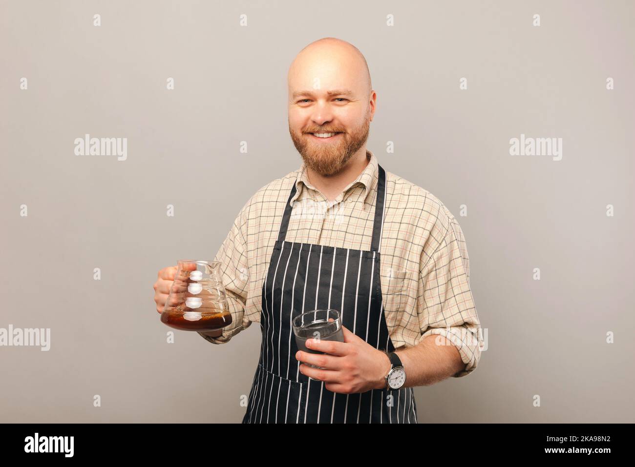 Young smiling barista man is holding a drip coffee server and a glass