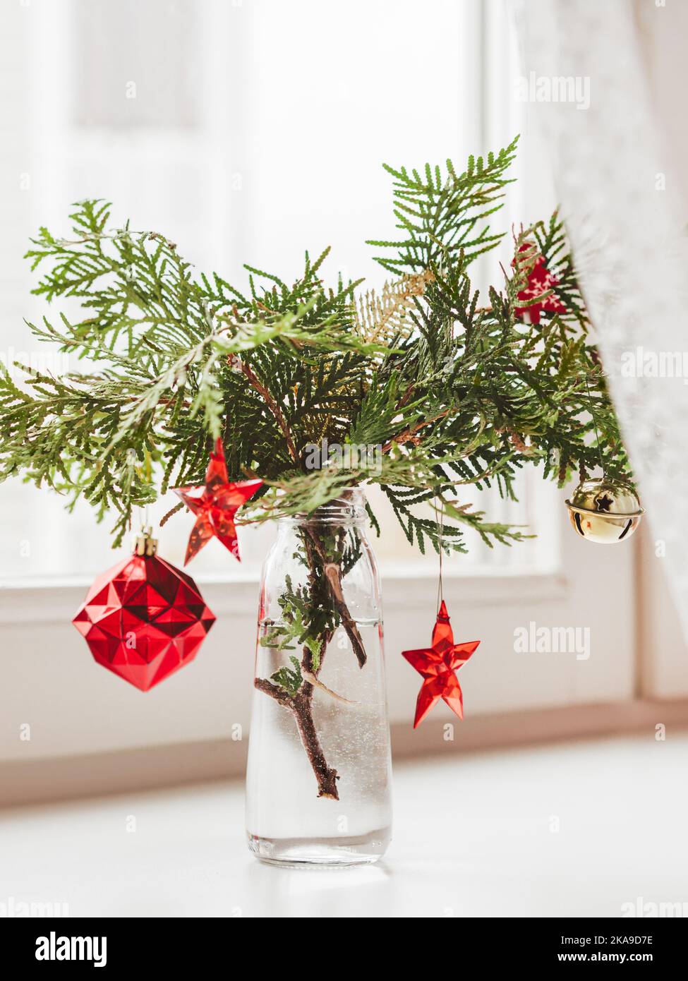 Vase with decorated thuja branches stands on window sill. Sustainable alternative for Christmas tree. Caring for nature. Refusal to cut down spruce fo Stock Photo