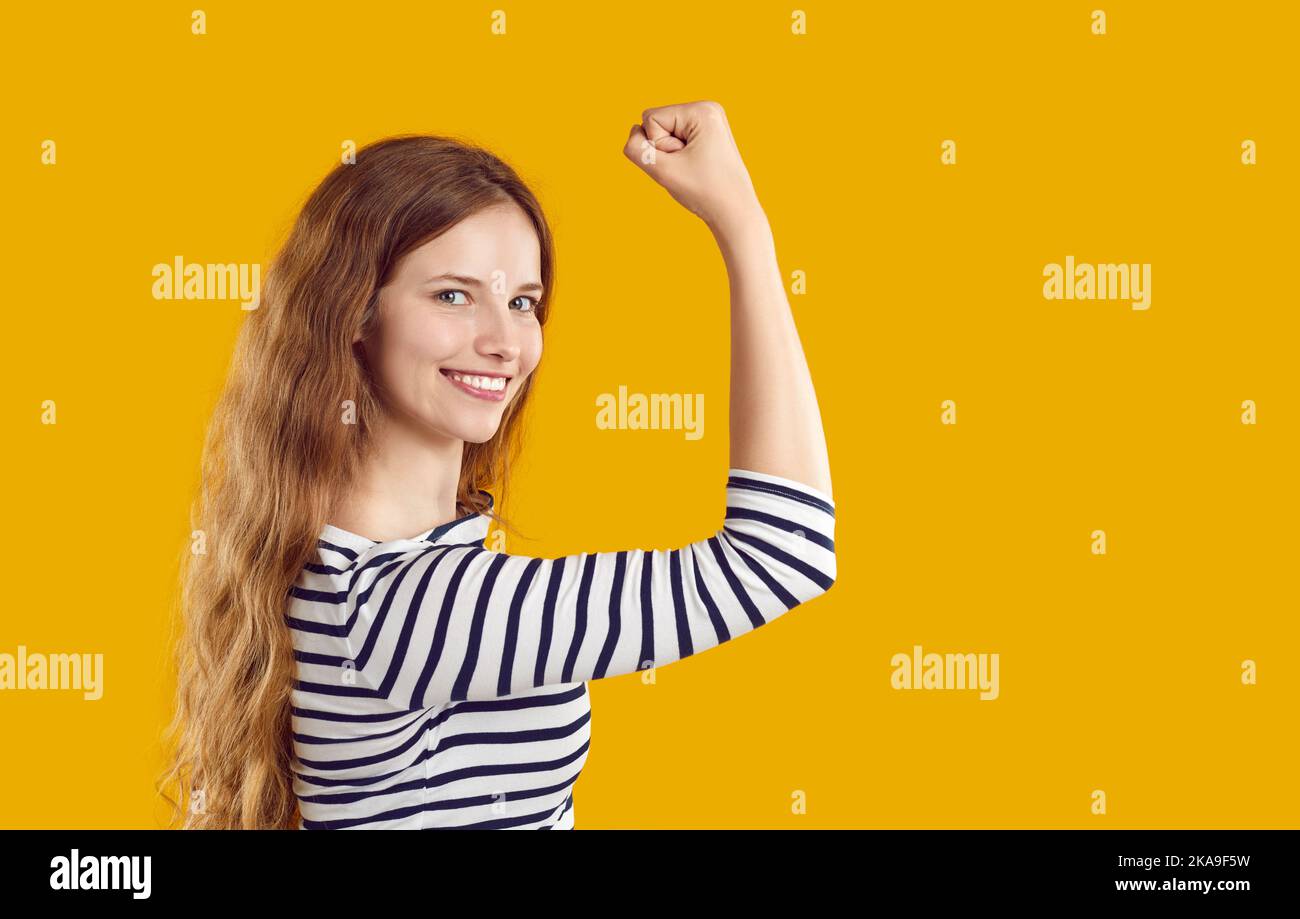 Happy confident strong young woman showing girl power, flexing her arm and smiling Stock Photo