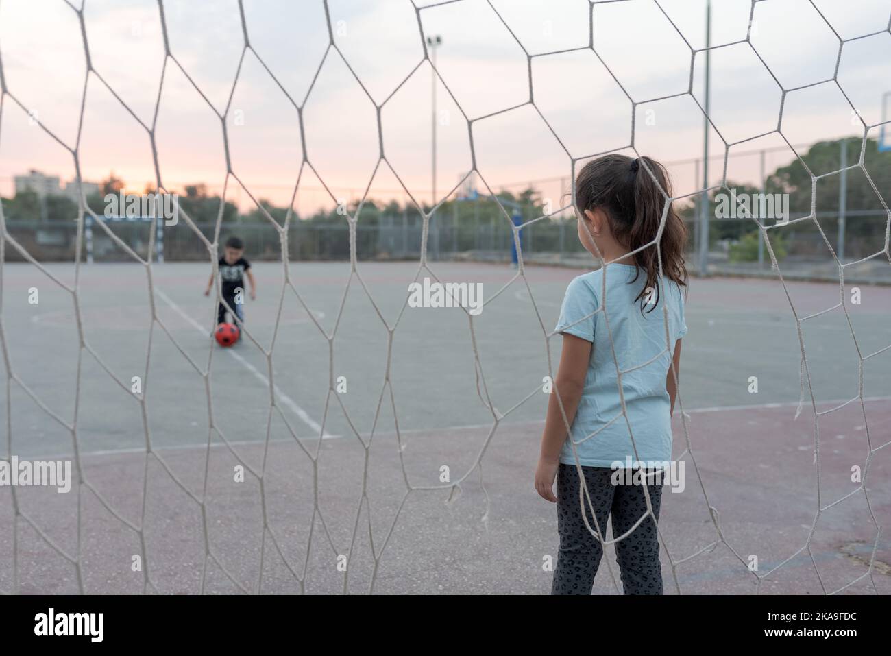 Back view of child goalkeeper ready to catch a soccer ball stand on soccer field in football goal. Selective focus on girl. Stock Photo