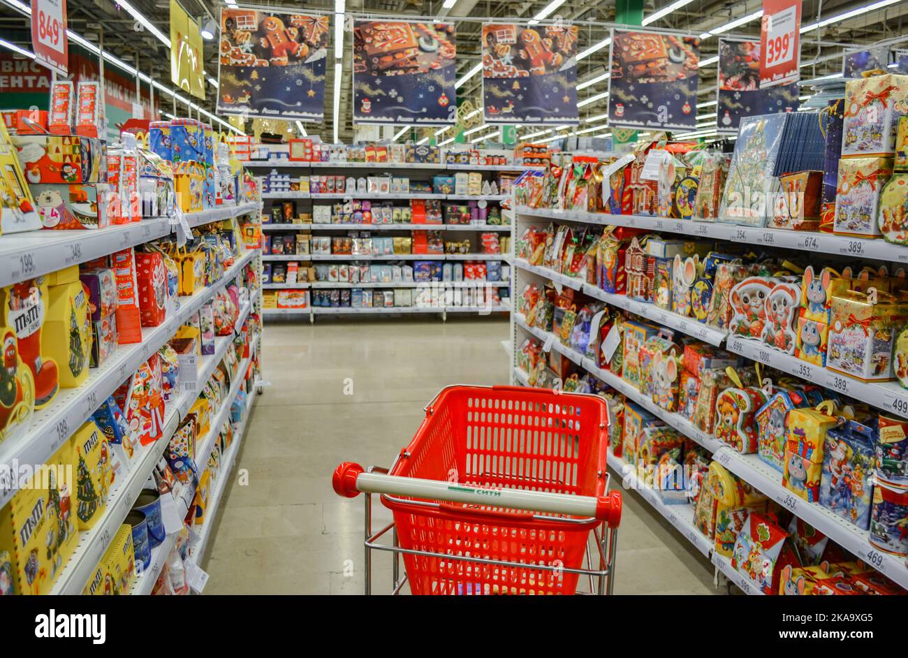 Moscow, Russia, November 2019: Red basket, supermarket trolley between the rows in the supermarket with Christmas sweets for children: chocolate figur Stock Photo