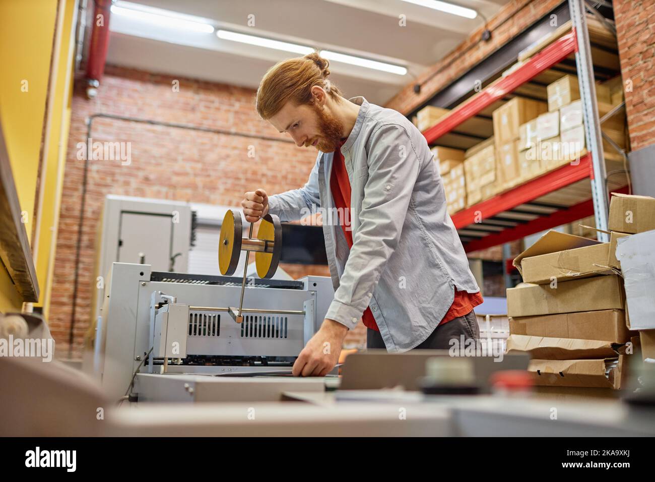 Side view portrait of young man setting up roller printing machine in industrial shop, copy space Stock Photo