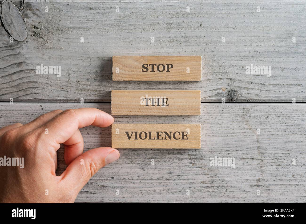 Male hand stacking three wooden pegs with a Stop the violence sign on them. Over simple white background. Stock Photo