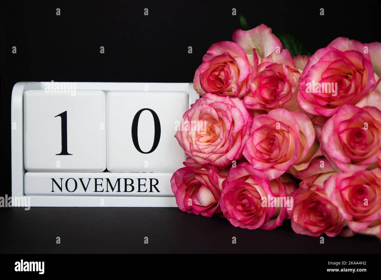 November 10 wooden calendar, white on a black background, pink roses lie nearby. Stock Photo
