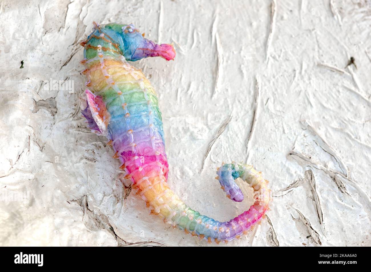 A figurine of a rainbow seahorse, lying on a white textured background Stock Photo