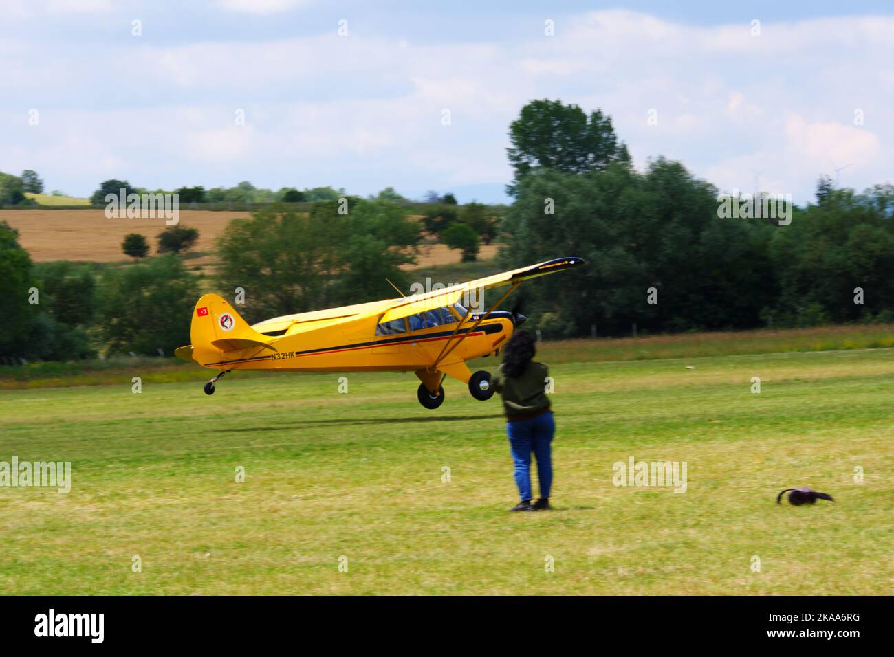 Yellow plane waiting on grass with people nearby in a sunny day outdoor Stock Photo