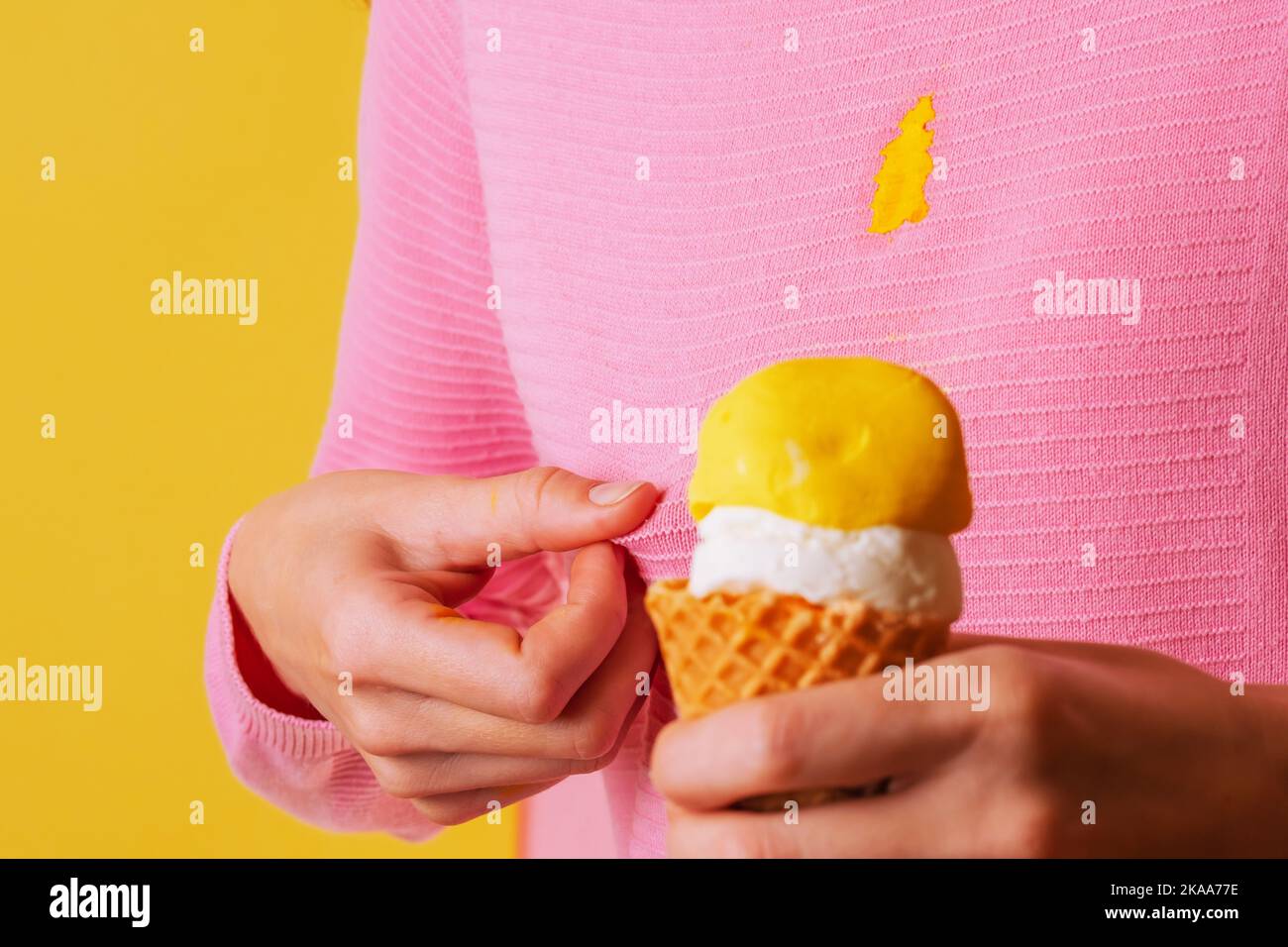 Female hand showing a dirty stain creamy banana ice cream on blouse. isolated. on a yellow background Stock Photo