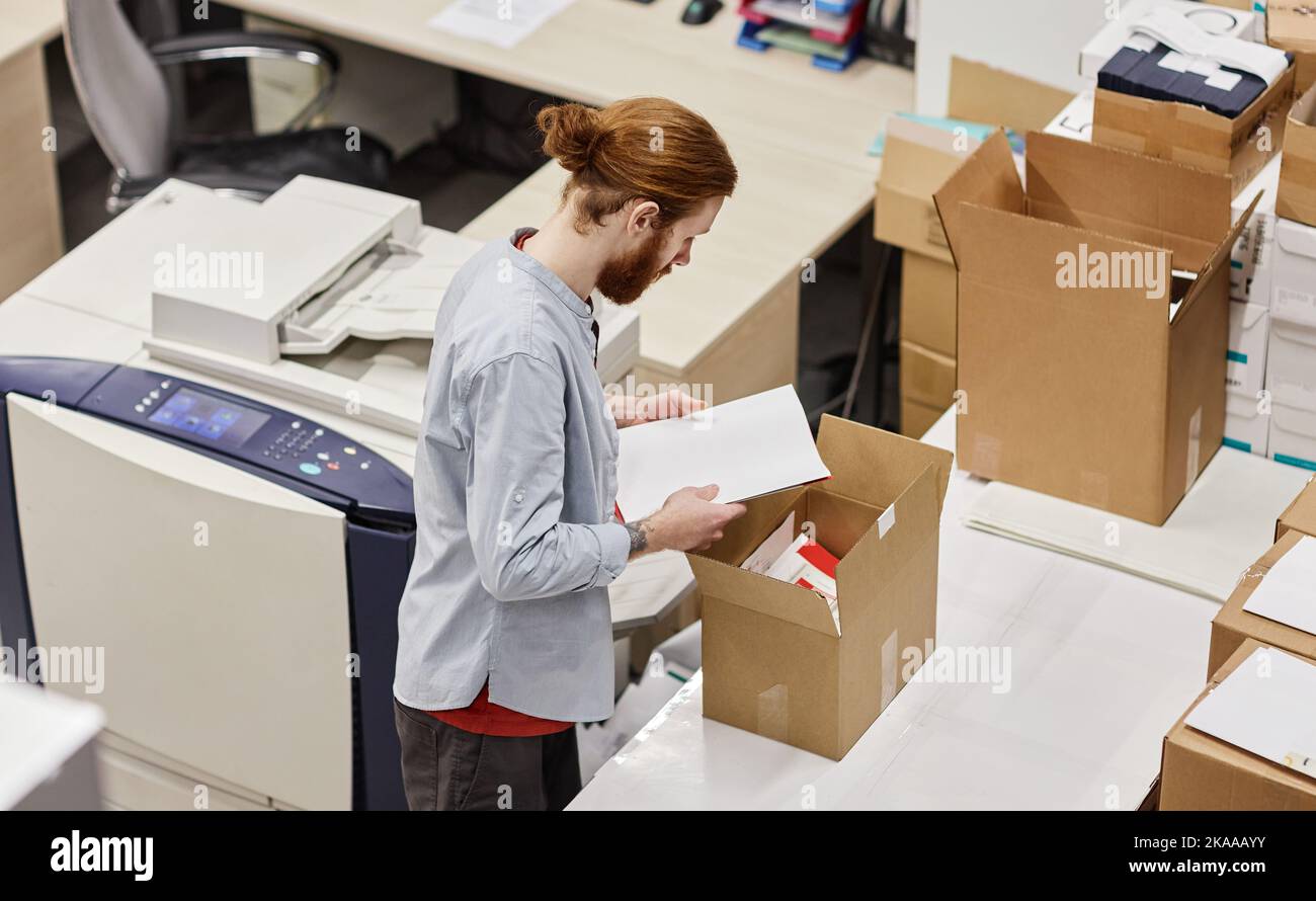 High angle portrait of young man packaging print products in publishing shop, copy space Stock Photo