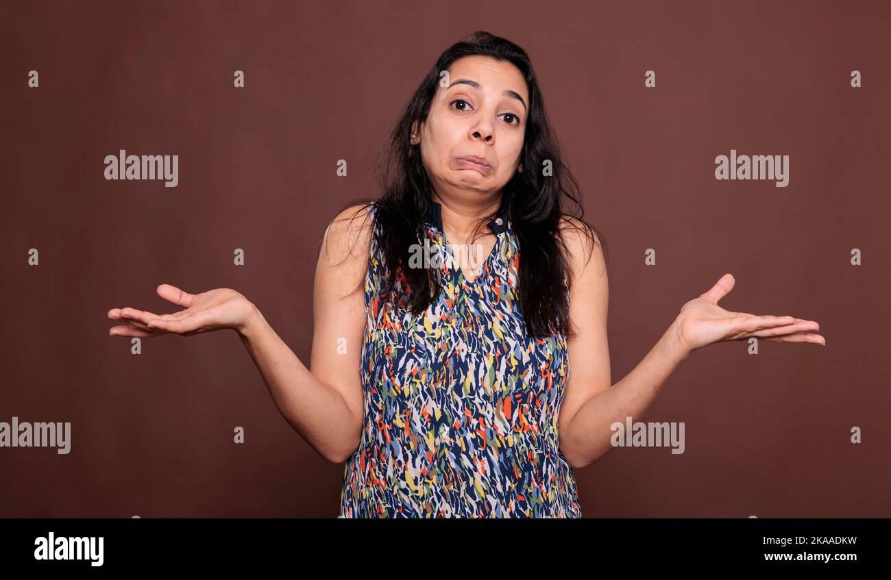 Confused indian woman shrugging shoulders with doubting facial expression, looking at camera. Puzzled lady standing with hands spread wide portrait, showing do not know gesture Stock Photo