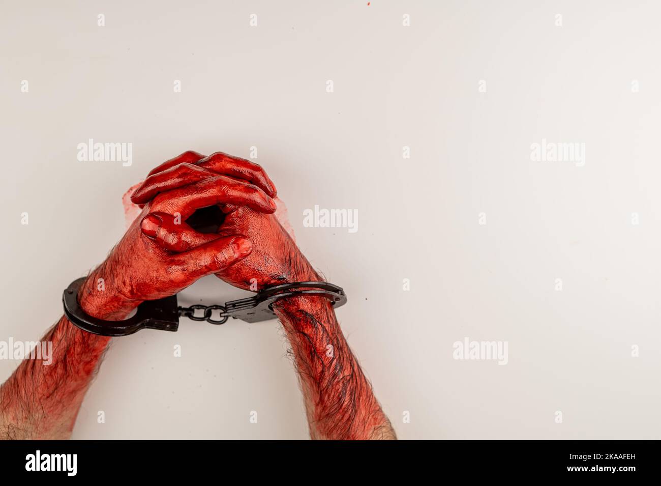 Bloodied male hands in handcuffs, folded on a white table. Stock Photo