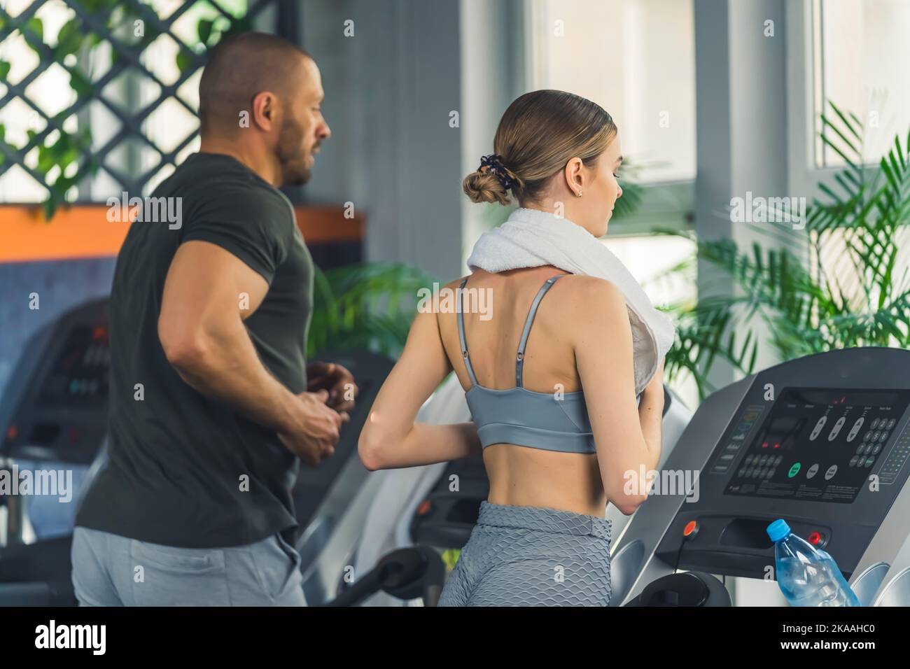 Cardio workout at nearby gym. Two caucasian people - muscular man in his late 30s and young skinny girl - running on modern treadmills. Gym interior. High quality photo Stock Photo