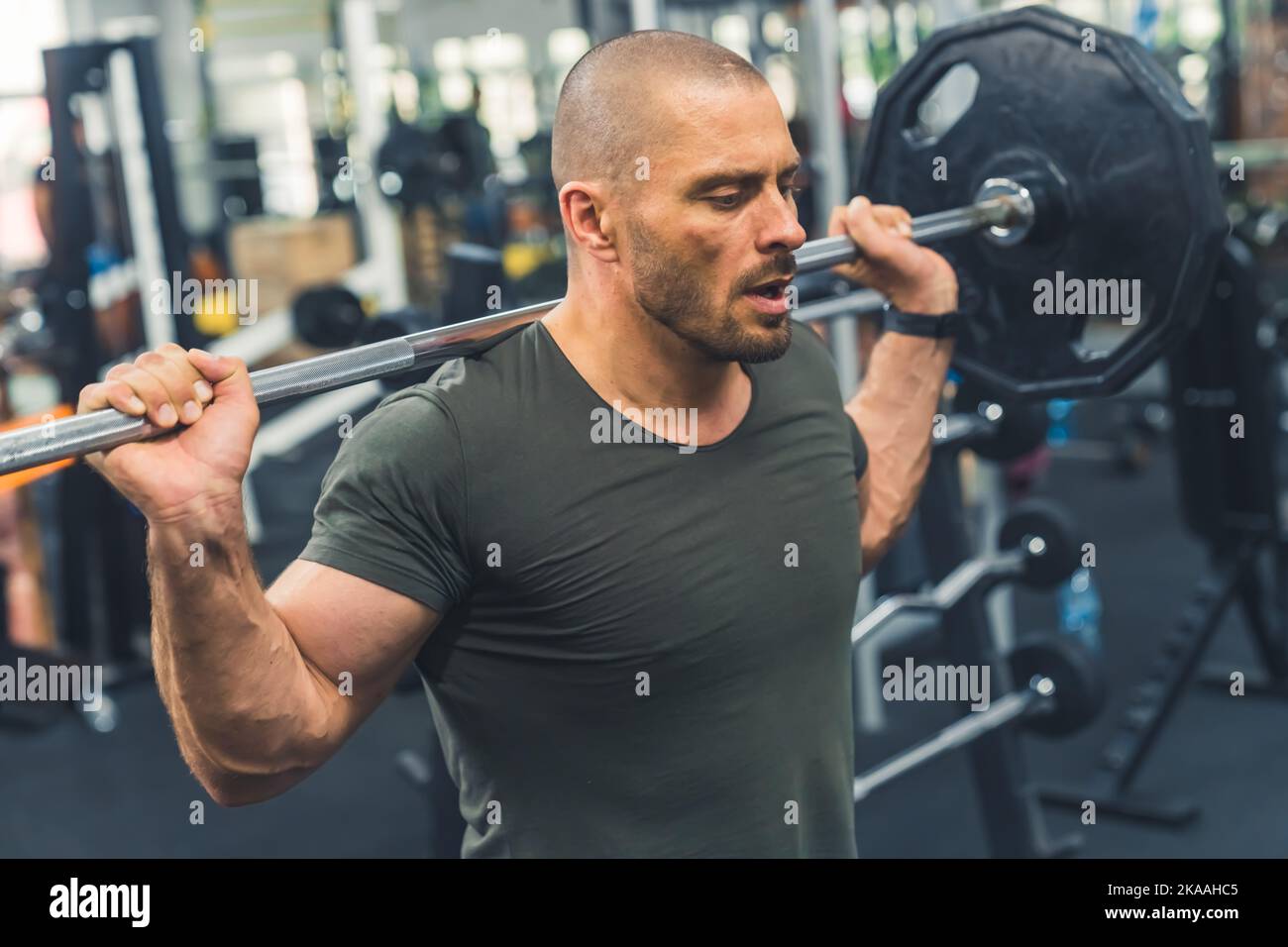 Power and determination. Medium indoor shot of focused middle-aged caucasian bald male bodybuilder lifting barbell. High quality photo Stock Photo