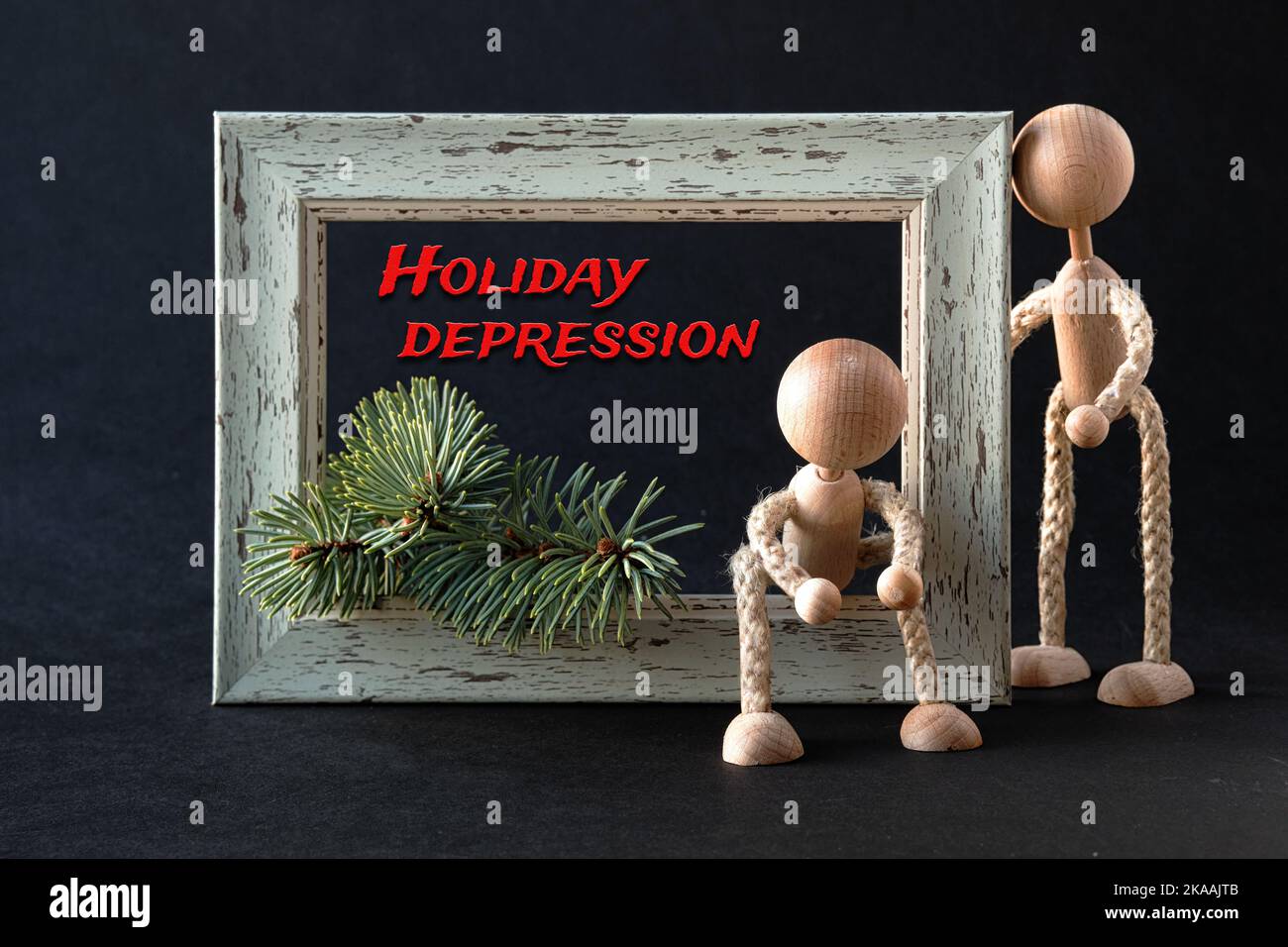 Holiday depression text. Mental disorder, despair. Wooden toy figurines, men by textured frame with fir twig and frosted pine cone. One man holds red Stock Photo