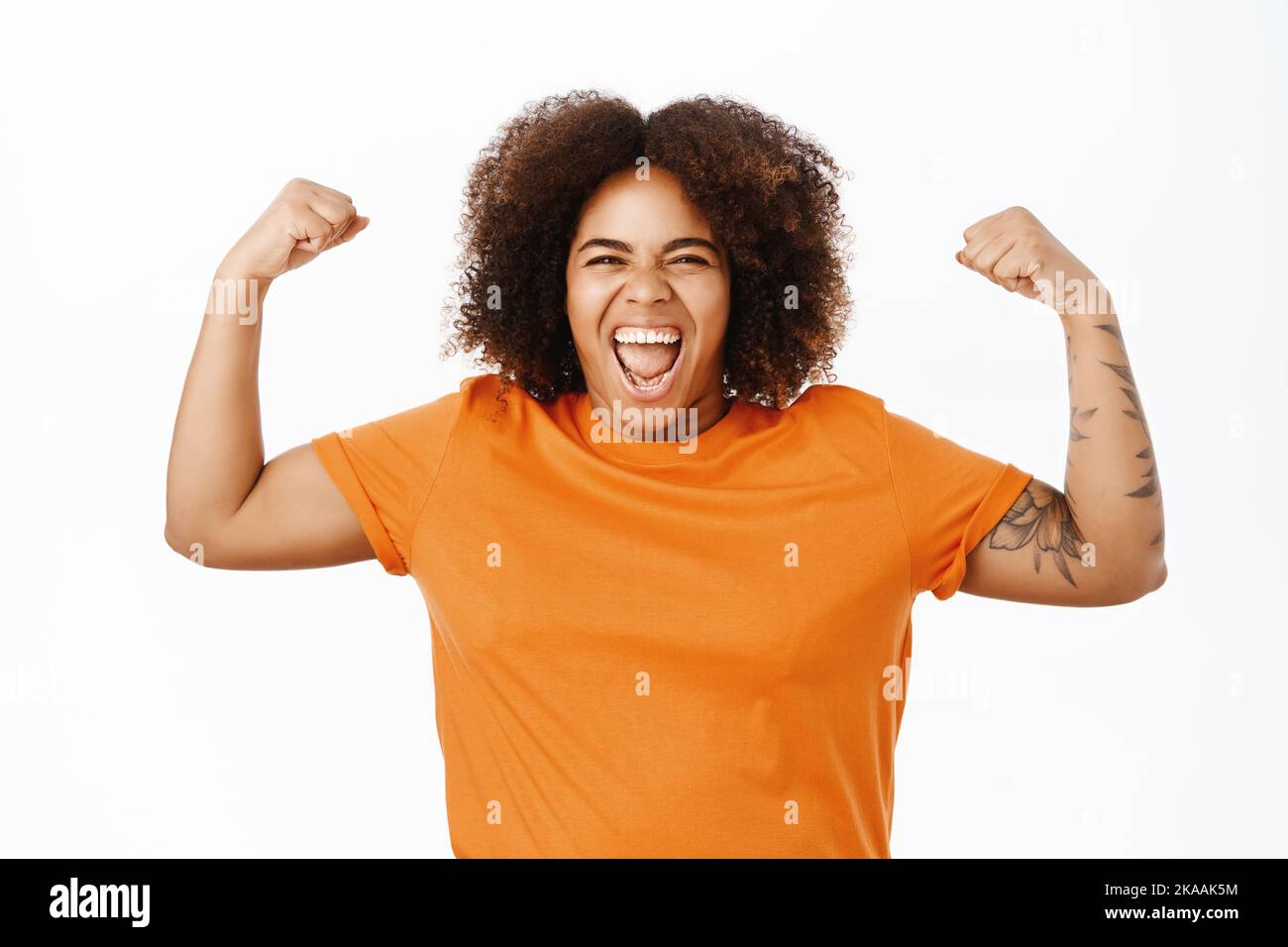 Portrait of confident and sassy african american woman, flexing biceps, raising arms and showing her strong muscles, feeling empowered, shouting Stock Photo