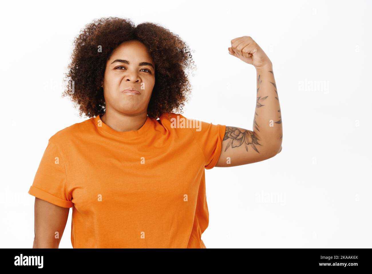 Girl power. Sassy young african american woman, flexing biceps, shows muscles strong arm, looking confident, standing over white background Stock Photo