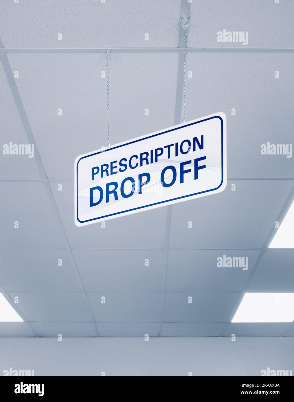 Plain white and blue prescription dropoff sign hanging from an interior ceiling of a pharmacy