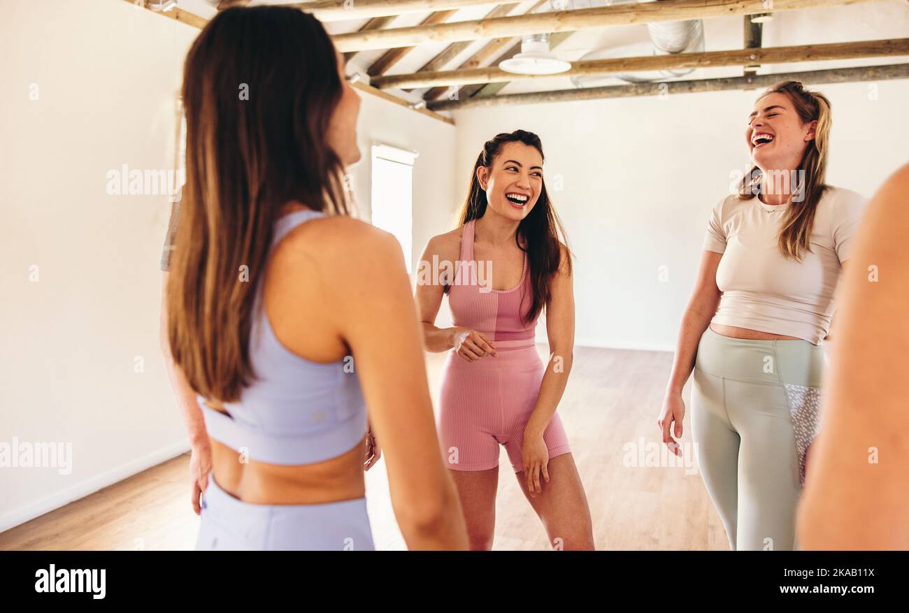 Female fitness friends laughing together while standing in a huddle. Group of women supporting each other in a community fitness centre. Happy young w Stock Photo