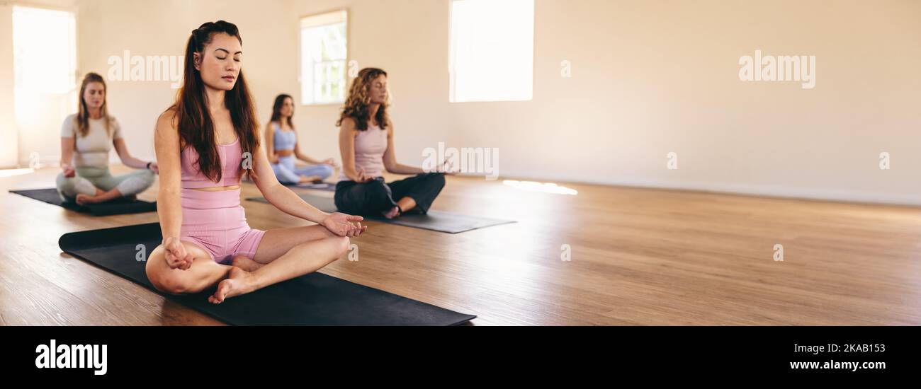 Group of diverse women meditating in sukhasana pose in a yoga class. Women of different ages practicing breathing exercises during a yoga session. Spo Stock Photo