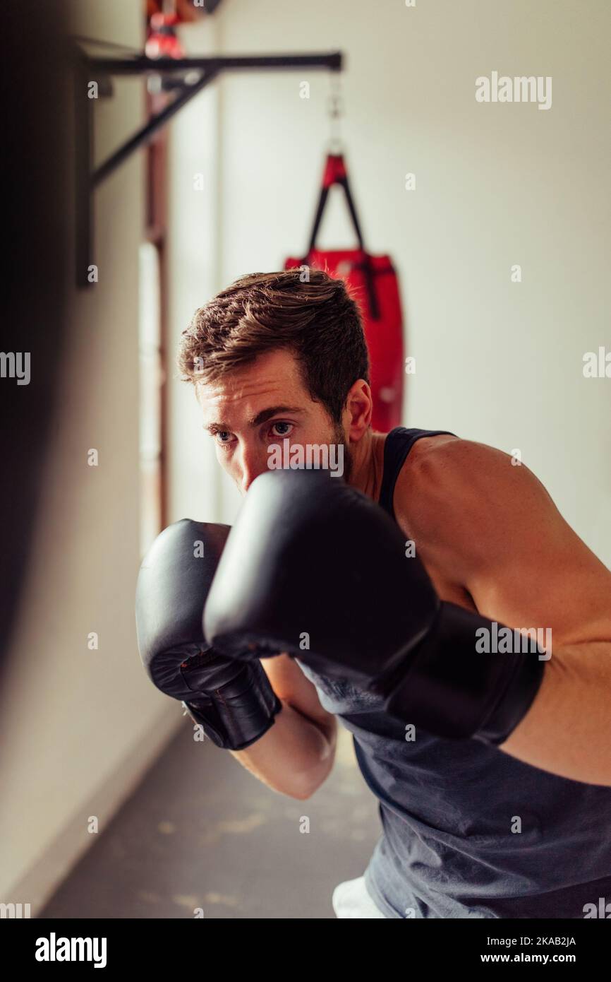 Solitary fighter training with boxing gloves at the gym. Determined young man practicing his punching techniques during a training session at the gym. Stock Photo