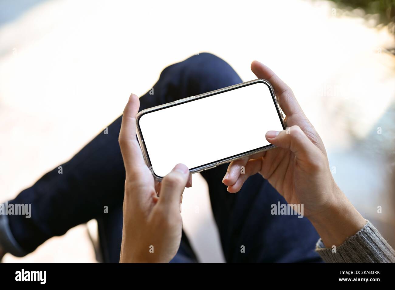 A smartphone white screen mockup in a horizontal position is in a male's hands. playing game, texting, watching video. cropped and close-up Stock Photo