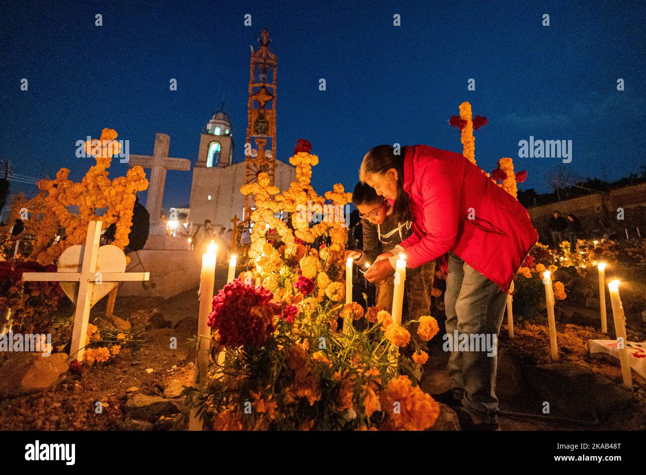 Morelia, Mexico, 1 Nov 2022, Mother and son light candles during the Day of the Dead celebration in the cemetery of Arocutin, Michoacan, Mexico. The indigenous Purepecha of this village prepare this annual ritual of remembrance by constructing altars with marigolds, candles and the favorite food or drink of the deceased.  The vigil takes place the night of November 1st and has become a major tourist attraction in the central Mexican state of Michoacan.  Brian Overcast/Alamy Live News Stock Photo