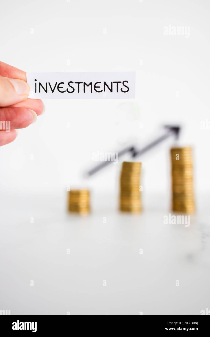 hand holding Investment text in front of growing stacks of coins with ...