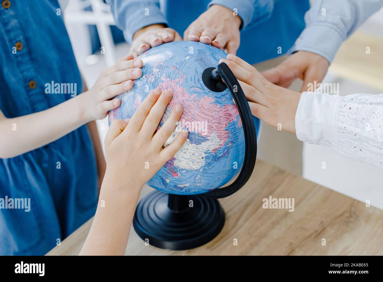 Touching to the Earth globe. Group of children of different ages stand in a spacious classroom at school with teacher touching the globe. Stock Photo
