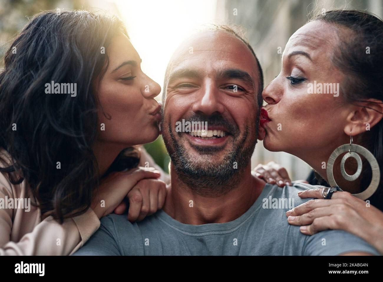 Kisses from my two favorite ladies. two women kissing their male friend on his cheeks. Stock Photo