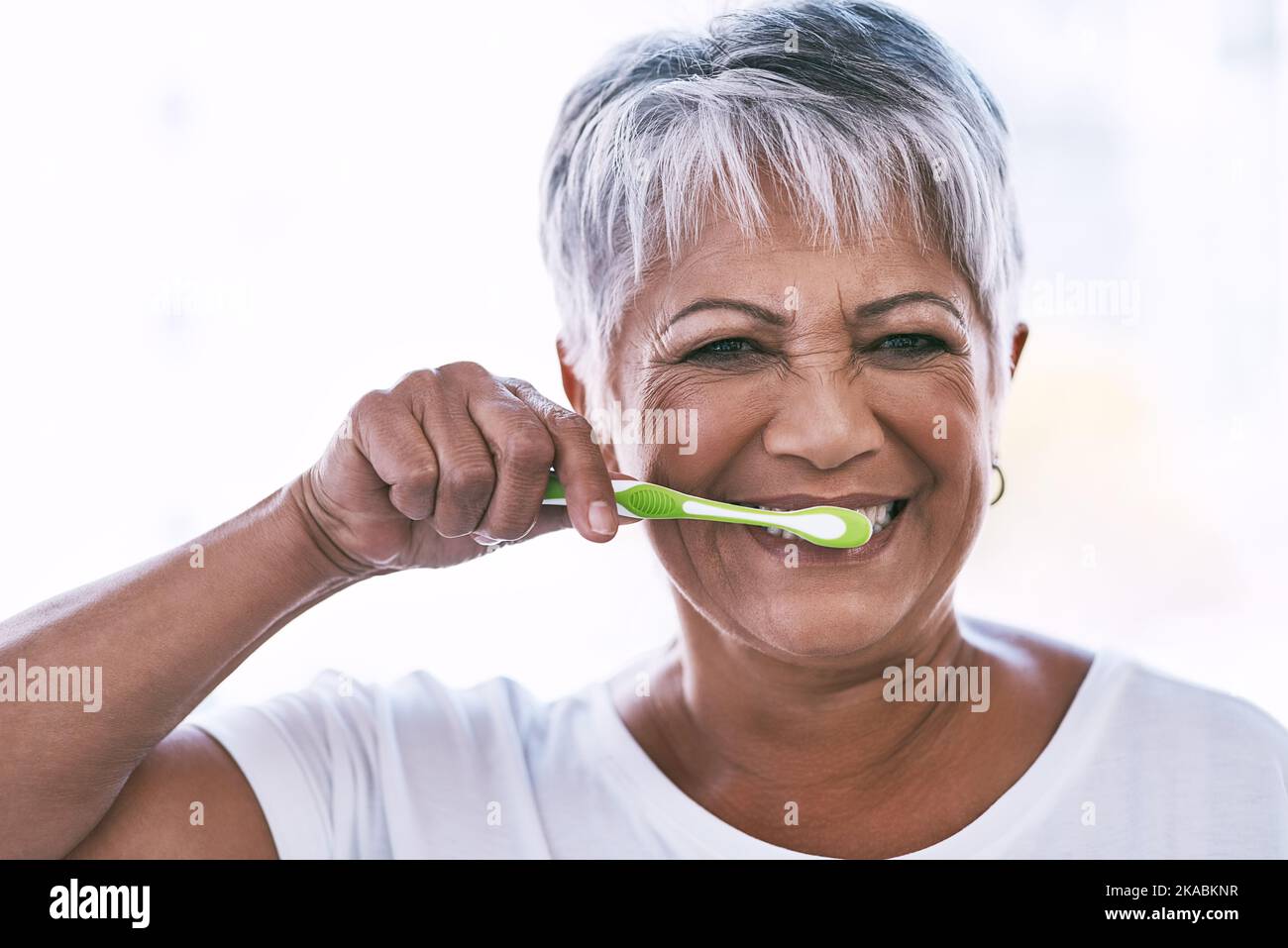 Going to have a great smile after this. Portrait of a cheerful mature woman brushing her teeth while looking at the camera at home. Stock Photo