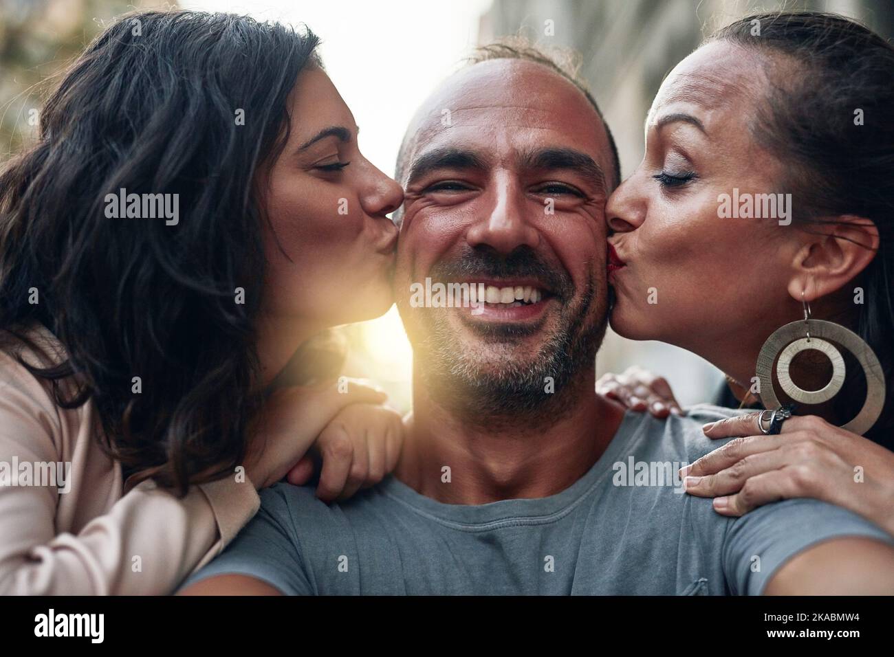 They are all the love I need. two women kissing their male friend on his cheeks. Stock Photo
