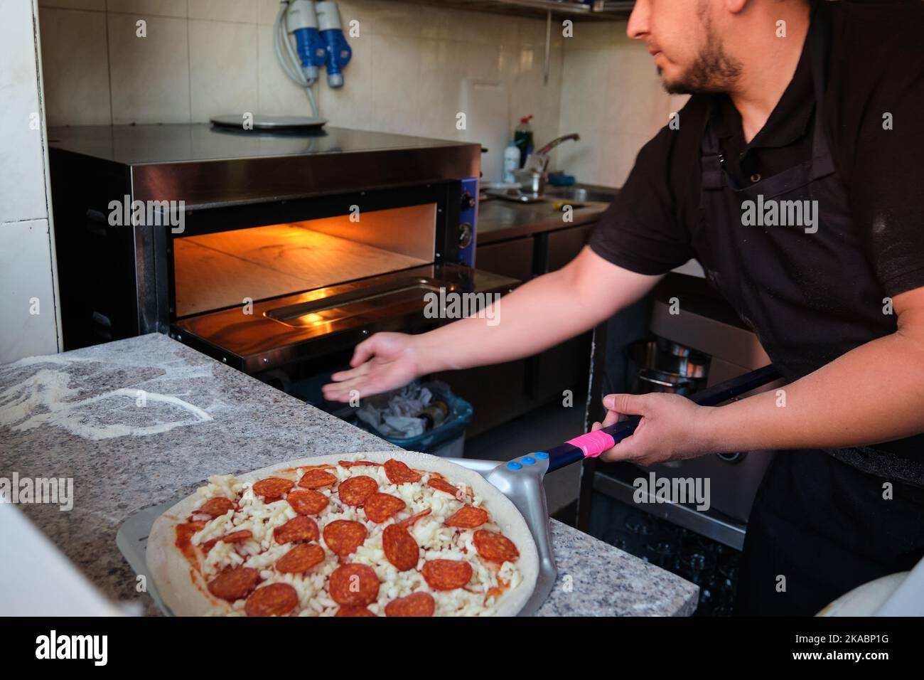 Latin man opening the oven to cook pepperoni pizza in a restaurant