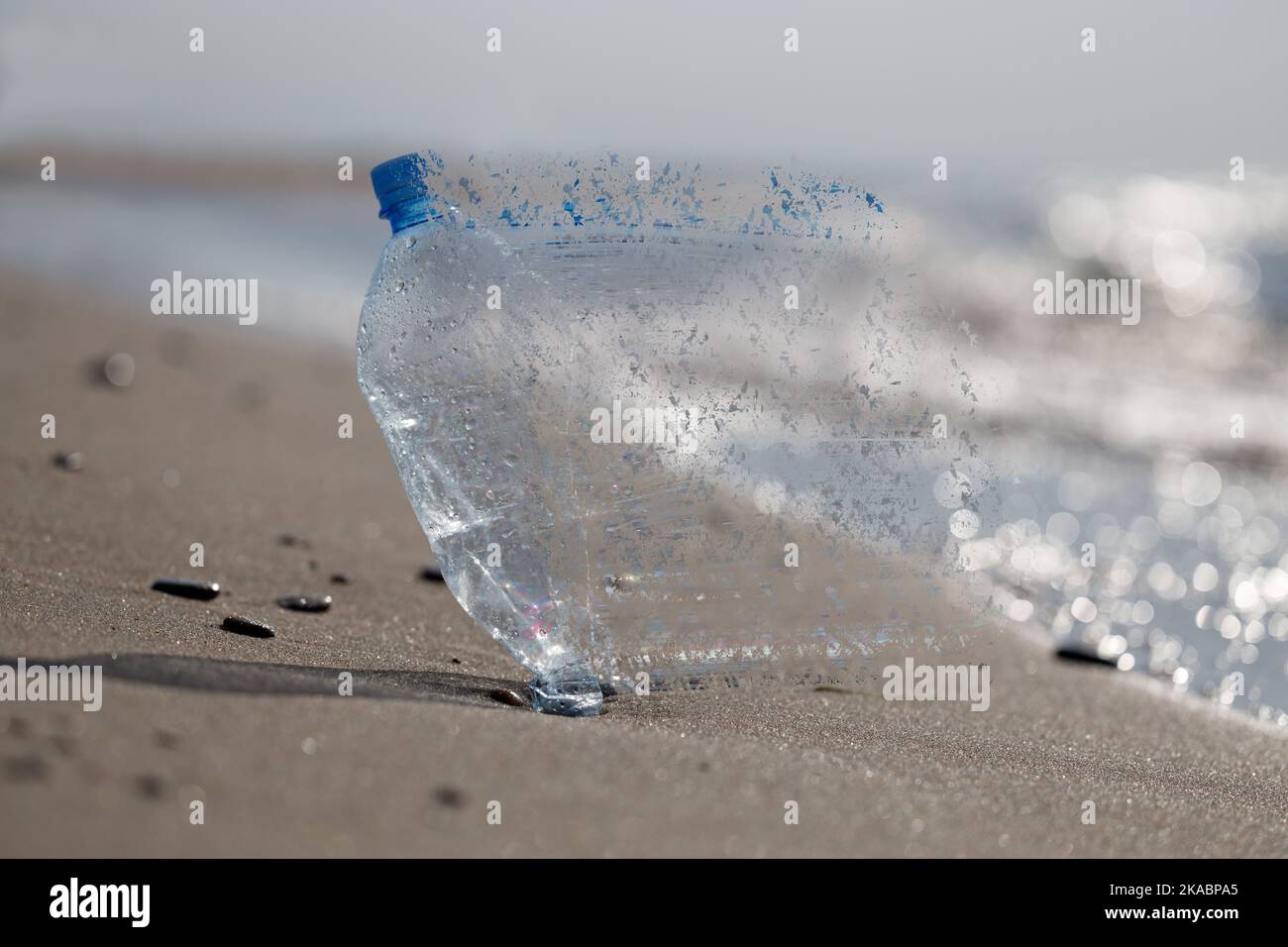 The problem of micro plastic pollution, conceptual image. Plastic bottle on the beach absorbed by the ocean. Stock Photo