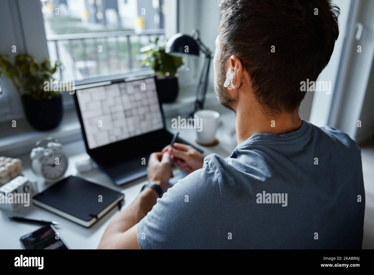 Home office workplace with laptop. Man working remotely from home, using laptop. Male freelancer sitting at table near window Stock Photo