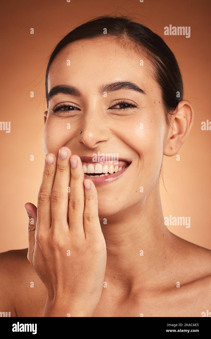 Skincare, hand and woman in studio for skin, makeup and beauty on orange background, happy and relax. Hand, portrait and face of indian wellness model Stock Photo