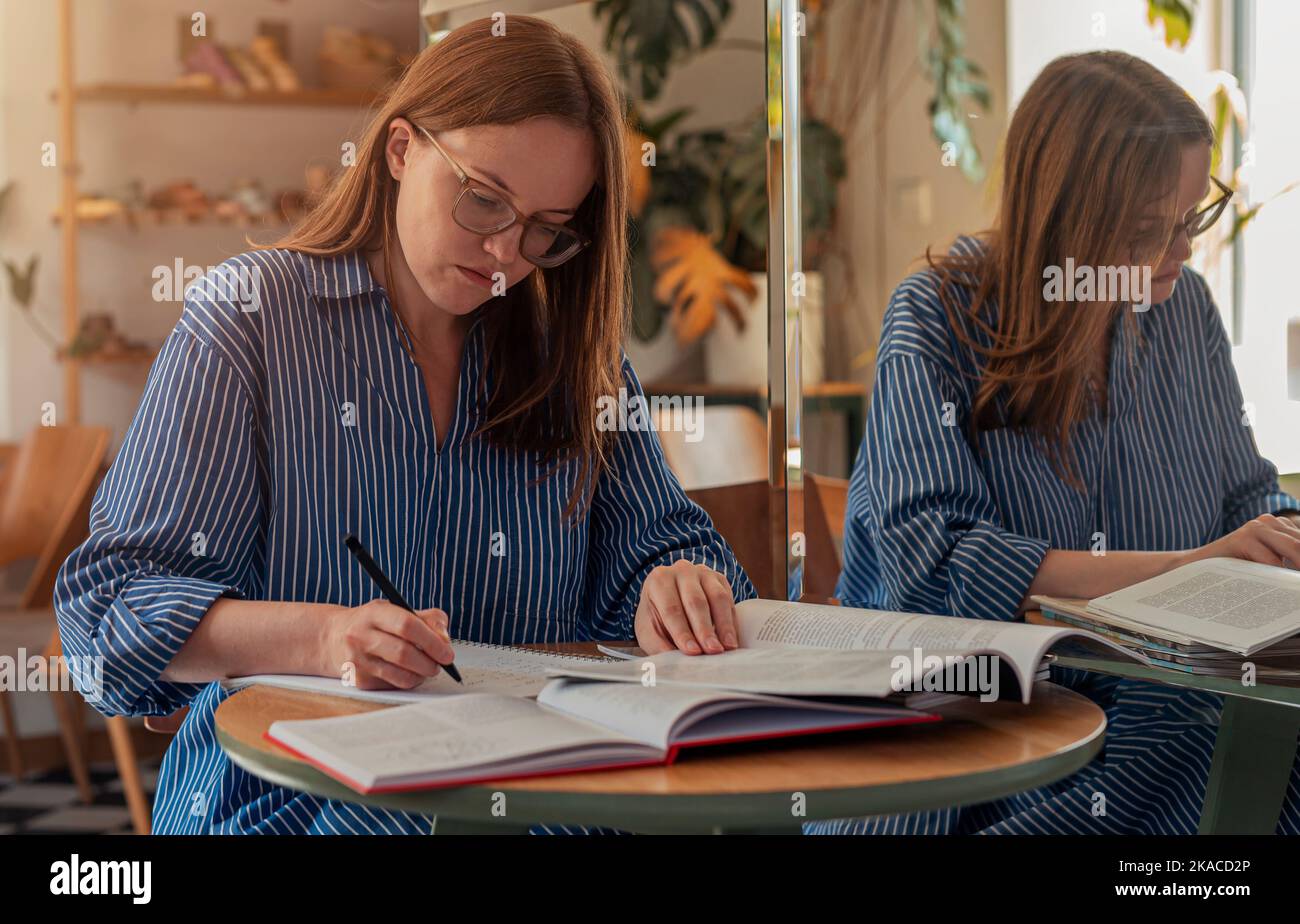 Smart student in glasses with books, writing smth, studying in coffee ...