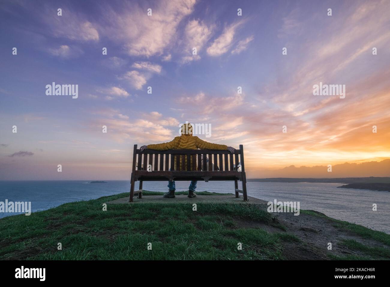 Man sitting on a bench overlooking the sea in cornwall at sunrise Stock Photo