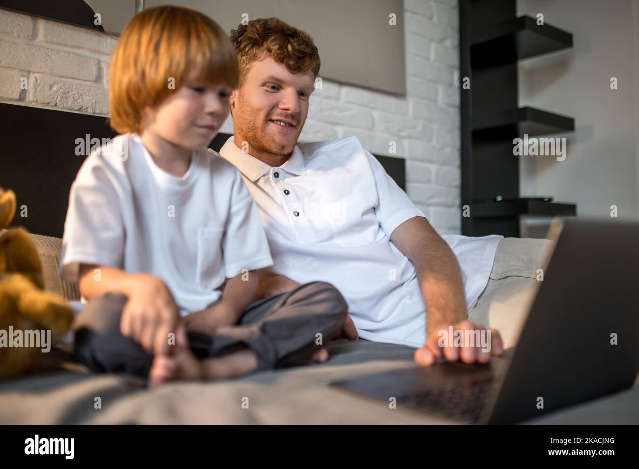 Dad working on a laptop while his son playing next to him Stock Photo
