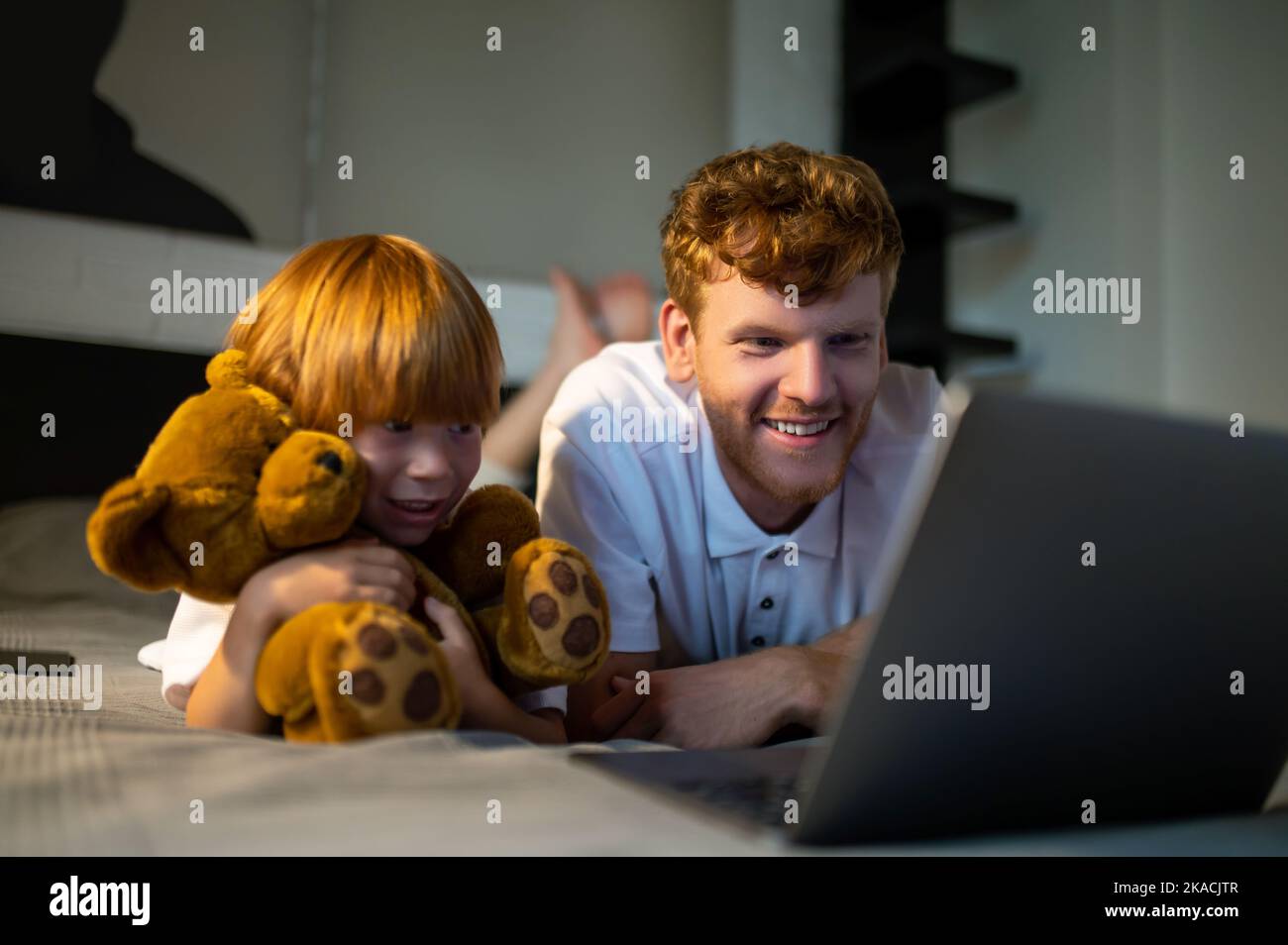 Father and son lying on bed and watching something on internet before going to sleep Stock Photo
