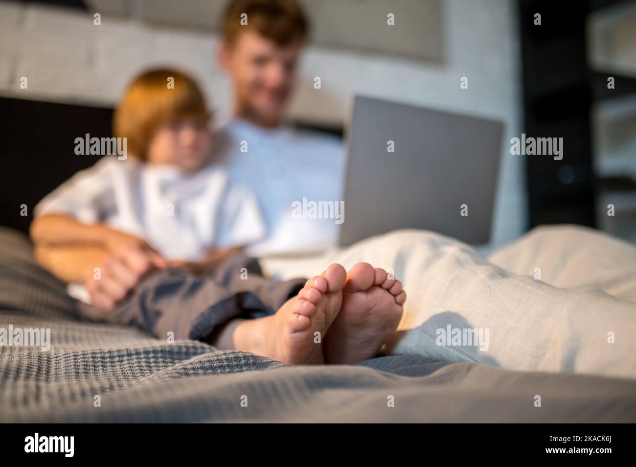Ginger man and his cute son lying in bed with their gadgets Stock Photo