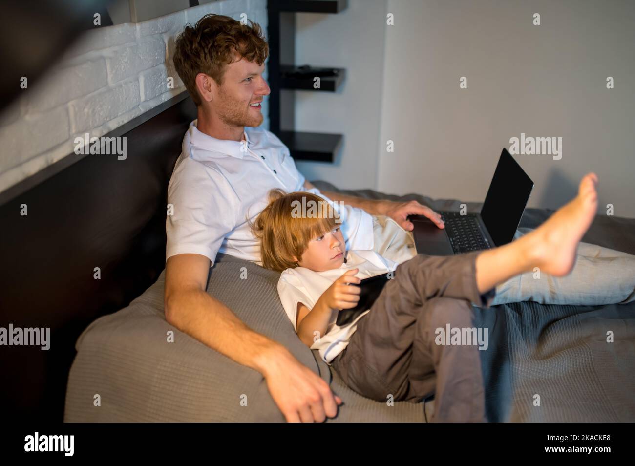 Father and son lying in bed and spending time on internet Stock Photo