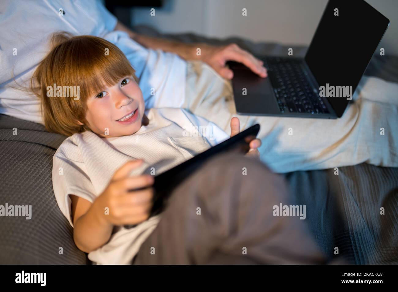 Father and son lying in bed and spending time on internet Stock Photo