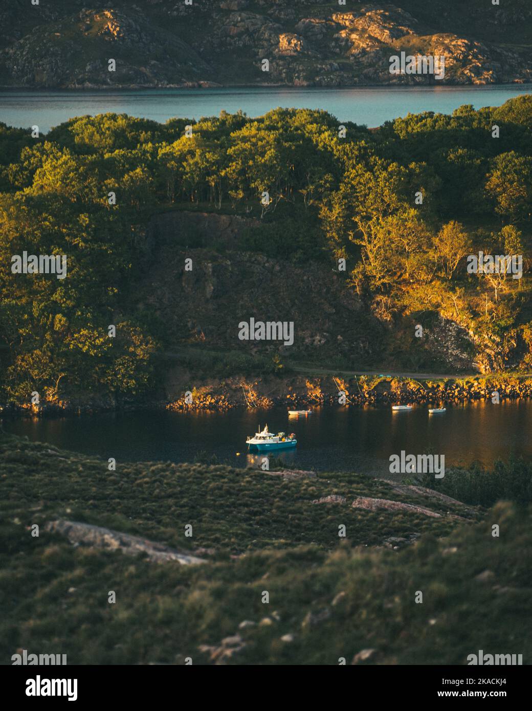 Tilt shifted image of a little blue fishing boat in a Loch in the Scottish Highlands during golden hour. Stock Photo
