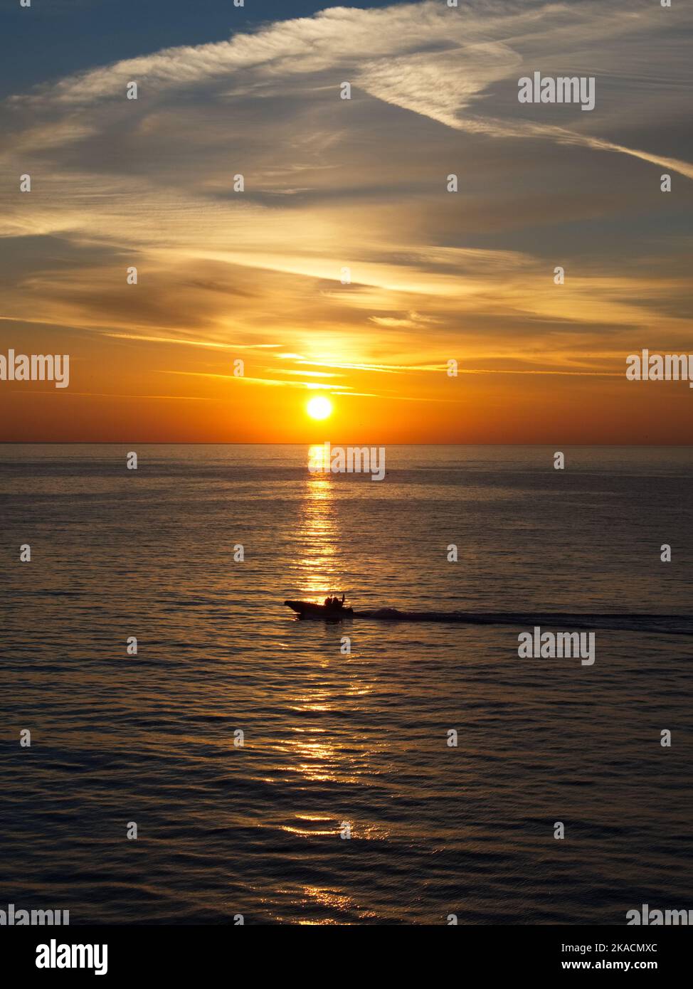 Portrait image of an orange sunrise at sea approaching Monaco with silhouette of speed boat in reflection of the sun across the water Stock Photo