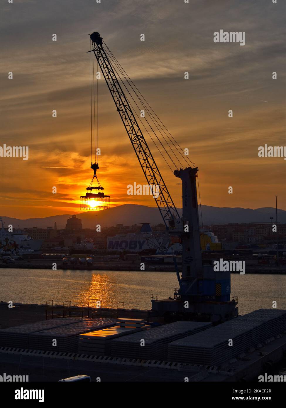 Orange sunrise over Pisa port silhouetted crane helps drag sun over the horizon Stock Photo