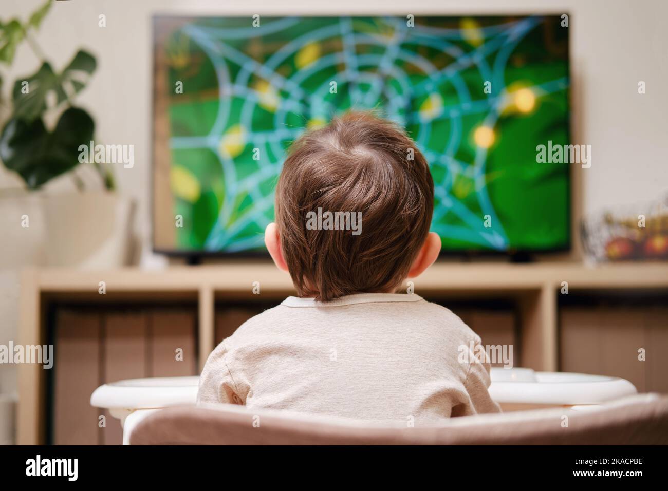 Happy toddler baby boy is watching cartoons on a big TV screen. A child