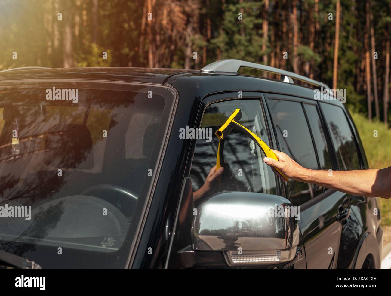 Hand with car rubber cleaner cleaning automobile window outdoors in summer. Stock Photo